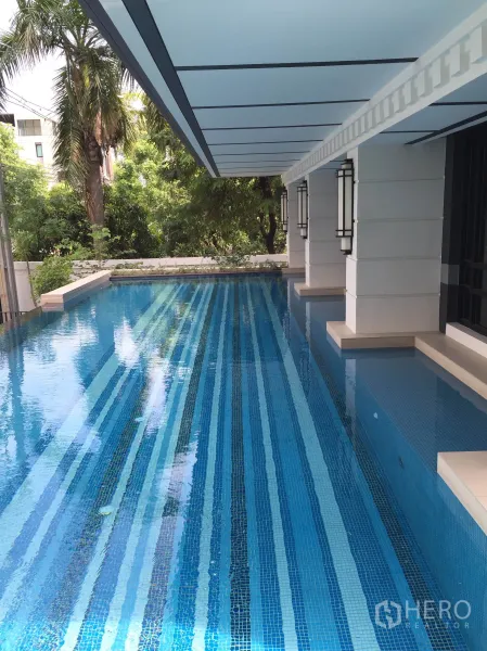 Condominium for rent in Pathum Wan, Bangkok - Outdoor lap pool with blue striped tiles beneath a covered deck beside lush trees.
