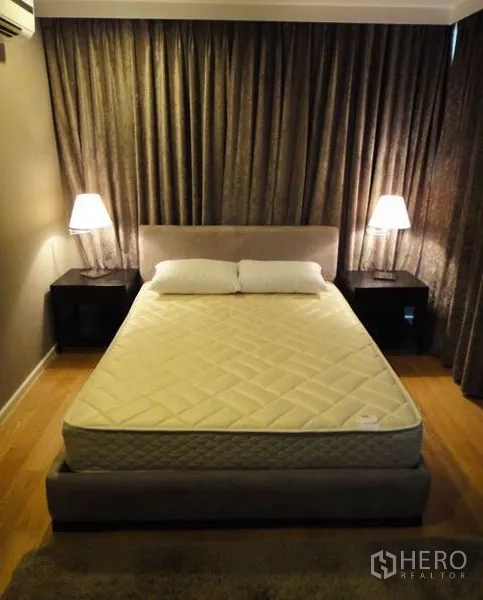 公寓 出租在Sathon, Bangkok - 静谧卧室，配大床、两侧床头柜与台灯，木地板与遮光窗帘。