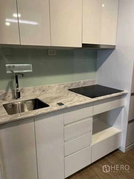Condominium for sale in Huai Khwang, Bangkok - Compact kitchen with marble countertop, sink and electric cooktop.