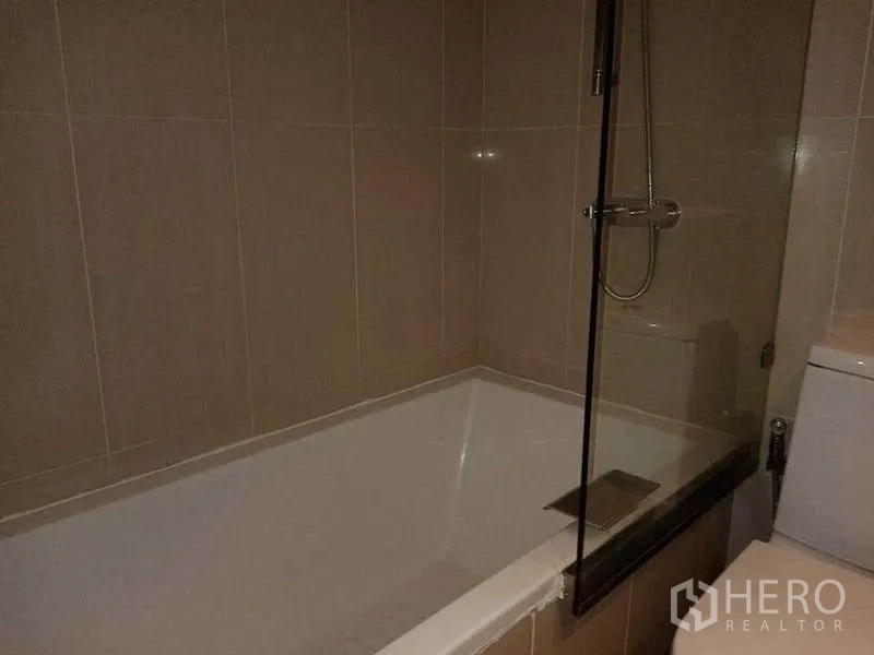 公寓 出租在Sathon, Bangkok - 浴室配浴缸与玻璃隔断，米色瓷砖墙面。