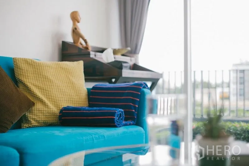 公寓 出售在Phra Khanong, Bangkok - 明亮客厅，蓝绿色沙发与彩色靠垫，带阳台景观的Bang Chak公寓。