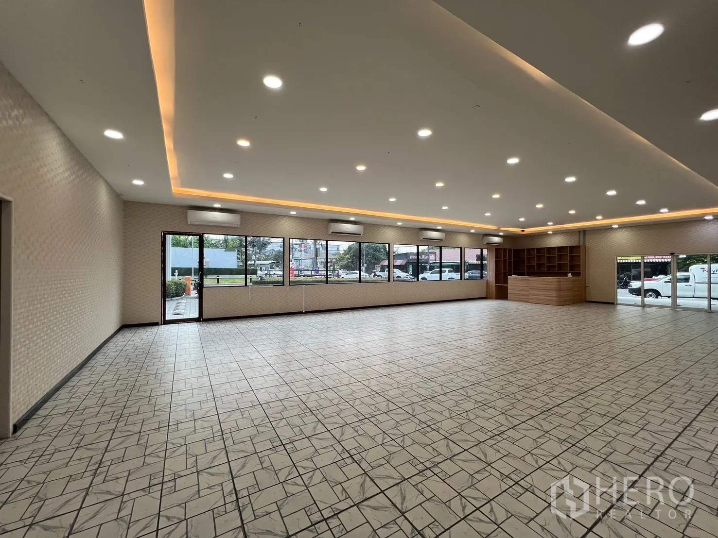 零售空间 for rent in Bueng Kum, Bangkok - 大开间展厅内景，灯带照明、瓷砖地面、周边窗户与通往街道的玻璃双门。