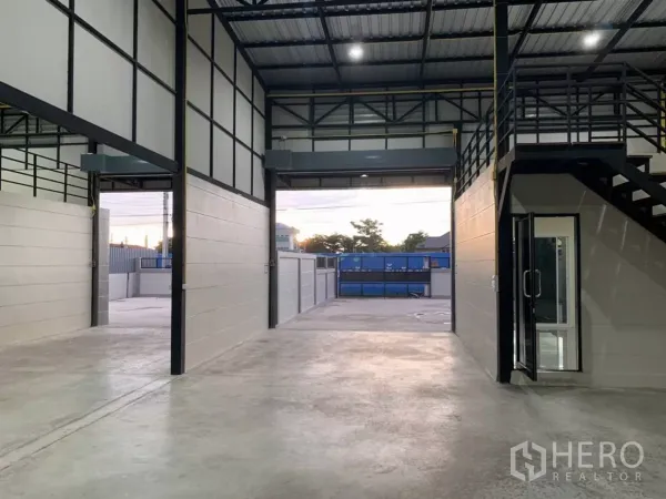 货栈 出租在Bang Bua Thong, Nonthaburi - 室内望向装卸院，见夹层平台、双卷闸与玻璃入口。