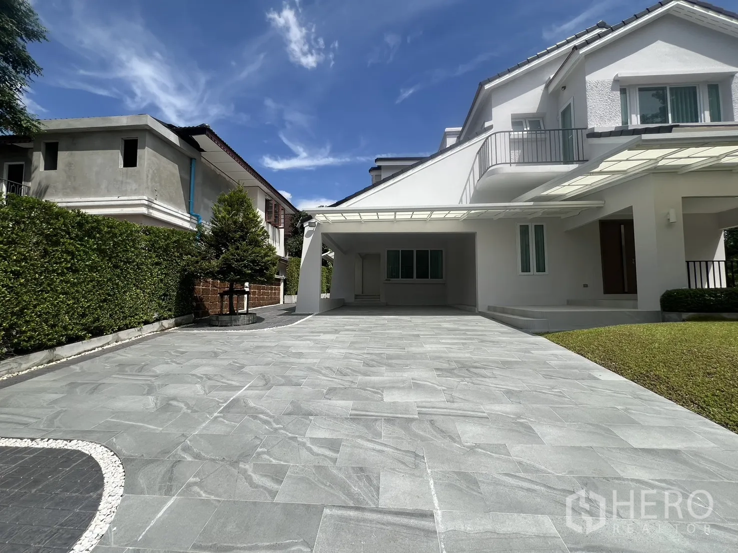 独立式住宅 出租在Mueang Samut Prakan, Samut Prakan - 宽车道通往车棚和阳台，绿篱围合。