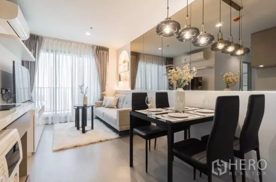 Condominium for rent in Chatuchak, Bangkok - Bright living and dining area of Life Ladprao 2‑bed condo with pendant lights, mirrored wall and sheer curtains to the balcony.