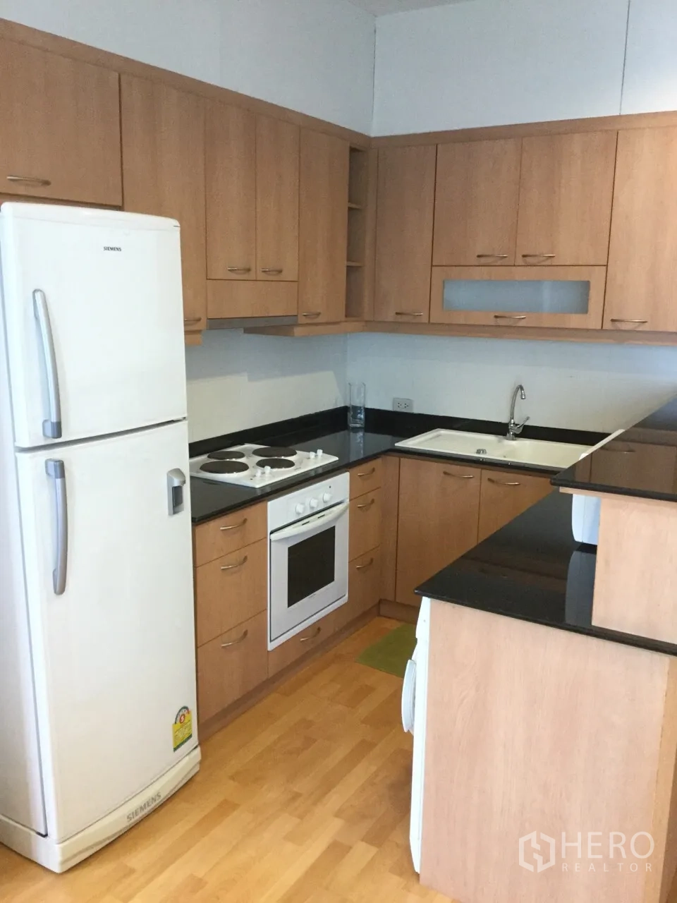 คอนโด ให้เช่าในKhlong Toei, Bangkok - ครัวรูปตัวแอล ตู้ไม้ เคาน์เตอร์หินสีดำ เตาอบ เตาไฟฟ้า และตู้เย็นสีขาว