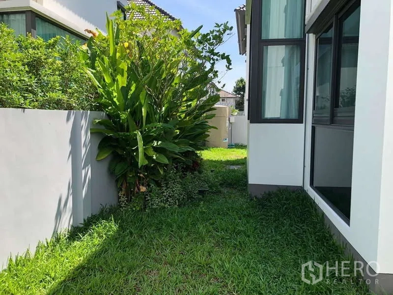 บ้าน ขายในBang Sao Thong, Samut Prakan - สนามหญ้าด้านข้างบ้าน พร้อมไม้พุ่มเขตร้อนและกำแพงรอบโครงการ