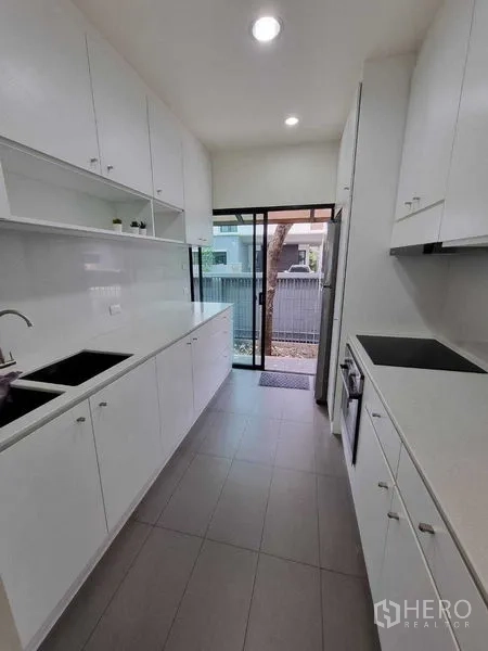 独立式住宅 出租或出售在Prawet, Bangkok - 狭长的一字型白色厨房，吊柜台面、水槽与后门。