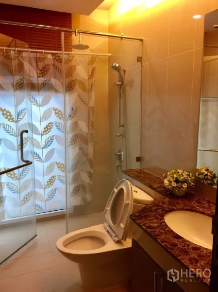 Condominium for rent in Watthana, Bangkok - Bathroom with glass-enclosed shower, rain and handheld heads, marble vanity and warm ambient lighting.