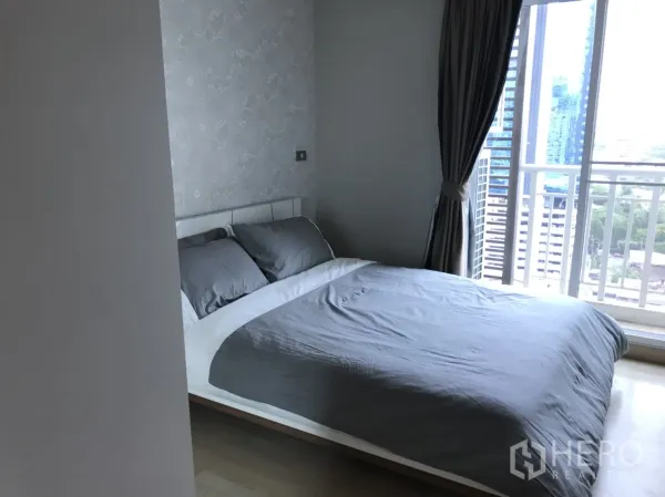 Condominium for rent in Watthana, Bangkok - Second bedroom with grey bedding, floor-to-ceiling window, curtains, and skyline view.