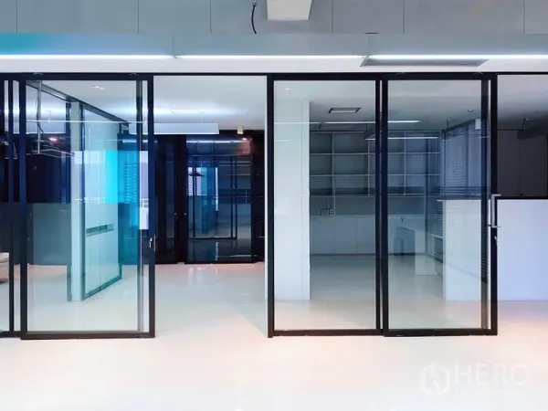 办公空间 出租在Phaya Thai, Bangkok - 一排黑框滑动玻璃门，分隔会议室与工作区的极简办公室。
