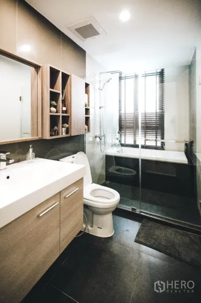 Condominium for rent in Huai Khwang, Bangkok - Modern bathroom featuring a wide vanity, toilet, glass-enclosed shower, and bathtub by the window.