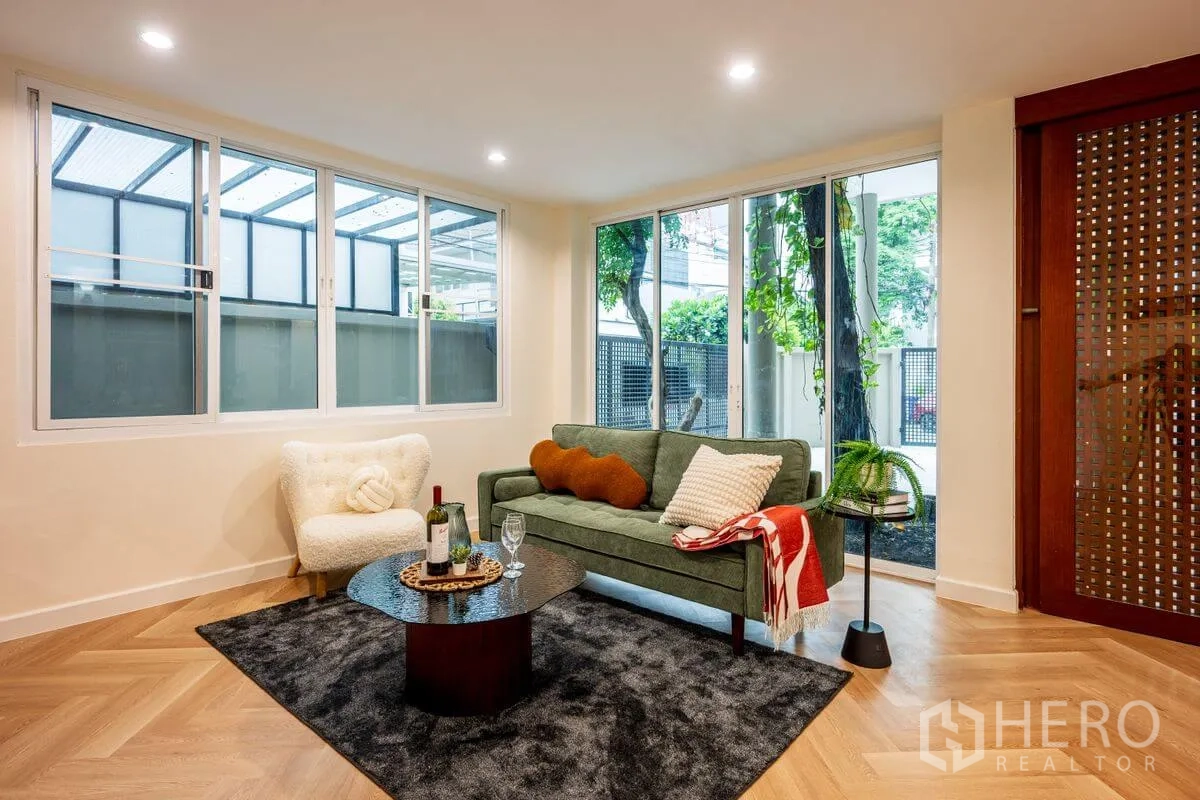 Detached House for rent or sale in Chatuchak, Bangkok - Cozy living area with green sofa, armchair, large windows, and wood lattice sliding door.