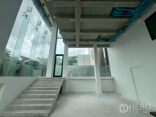 พื้นที่ขายปลีก ให้เช่า - ภายในชั้นล่างเพดานสูง พร้อมบันไดคอนกรีตและผนังกระจกเต็มความสูง