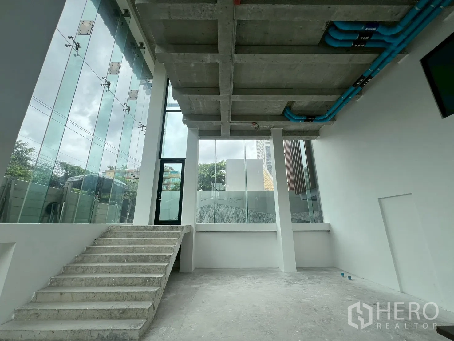 พื้นที่ขายปลีก ให้เช่า - ภายในชั้นล่างเพดานสูง พร้อมบันไดคอนกรีตและผนังกระจกเต็มความสูง