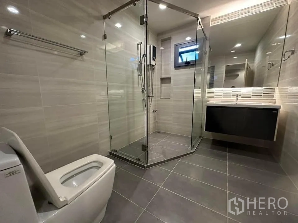 Detached House for rent in Bang Kapi, Bangkok - Modern bathroom with grey tiles, glass shower and floating vanity.