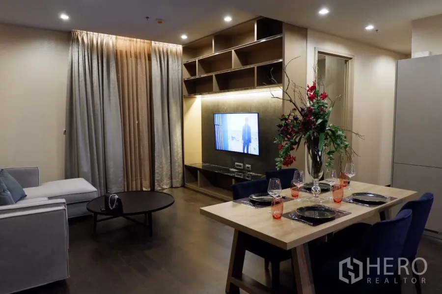 公寓 出租在Watthana, Bangkok - 开放式客餐厅，内置电视墙与搁架，木地板，落地窗帘，氛围温馨。