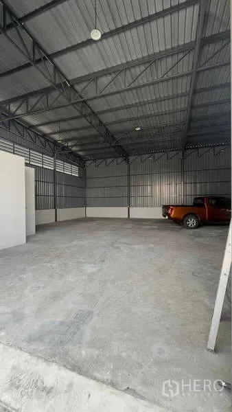 货栈 出租在Bang Khen, Bangkok - 仓库内部空间开阔，钢结构桁架屋顶与混凝土地面，旁边停有皮卡车。