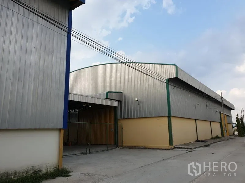 Warehouse for rent in Lat Krabang, Bangkok - Corner view of a large steel-clad warehouse with green trim and a gated loading entrance.