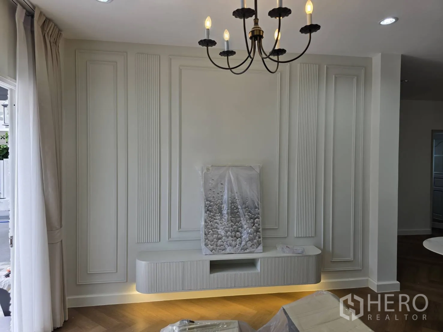 Detached House for sale in Lam Luk Ka, Pathum Thani - Living room with paneled feature wall, floating TV console with underlighting, and chandelier.