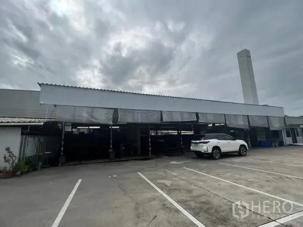 ที่ดิน ให้เช่าในBang Na, Bangkok - ลานคอนกรีตในบางนา พร้อมหลังคาจอดรถยาว มีรถเอสยูวีสีขาว และปล่องระบายอากาศสูง