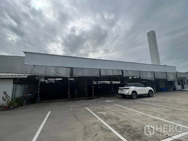 ที่ดิน ให้เช่าในBang Na, Bangkok - ลานคอนกรีตในบางนา พร้อมหลังคาจอดรถยาว มีรถเอสยูวีสีขาว และปล่องระบายอากาศสูง
