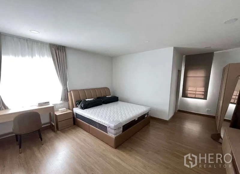 Detached House for rent in Bang Phli, Samut Prakan - Spacious bedroom with upholstered bed, work desk, large curtained window and wood flooring