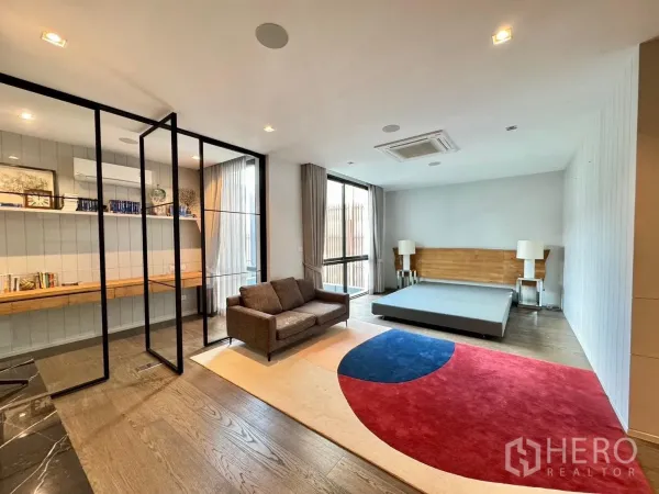 Detached House for rent or sale in Prawet, Bangkok - Open bedroom suite with glass partition, sofa, platform bed and built-in desk.