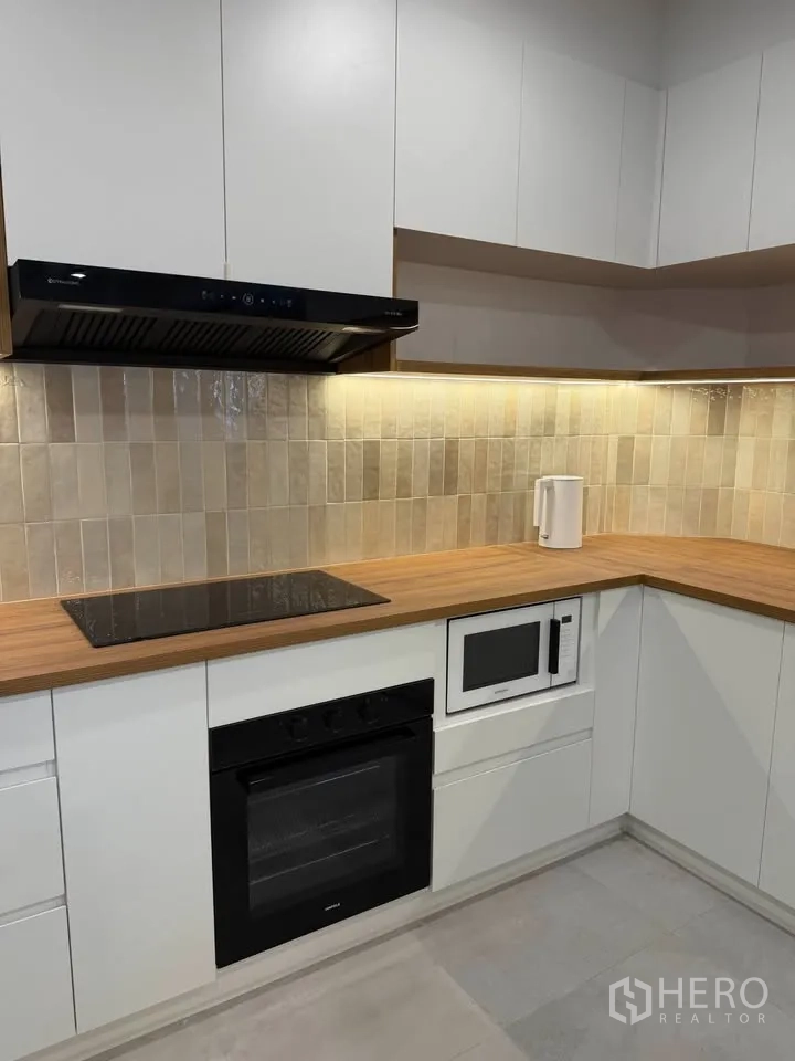 Condominium for rent in Watthana, Bangkok - Corner kitchen with cooktop, oven, microwave, and wood countertops.