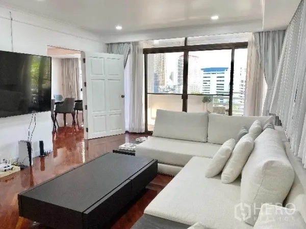 คอนโด ให้เช่าในKhlong Toei, Bangkok - ห้องนั่งเล่นพร้อมโซฟาตัวแอล ทีวีติดผนัง และหน้าต่างเต็มบานเชื่อมระเบียงชมวิวเมือง