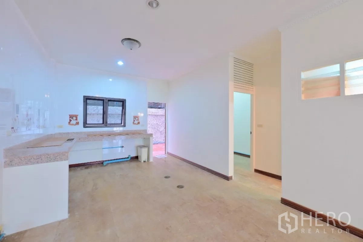 Townhouse for sale in Watthana, Bangkok - Kitchen area with L-shaped granite counter, window, and door to the rear terrace.