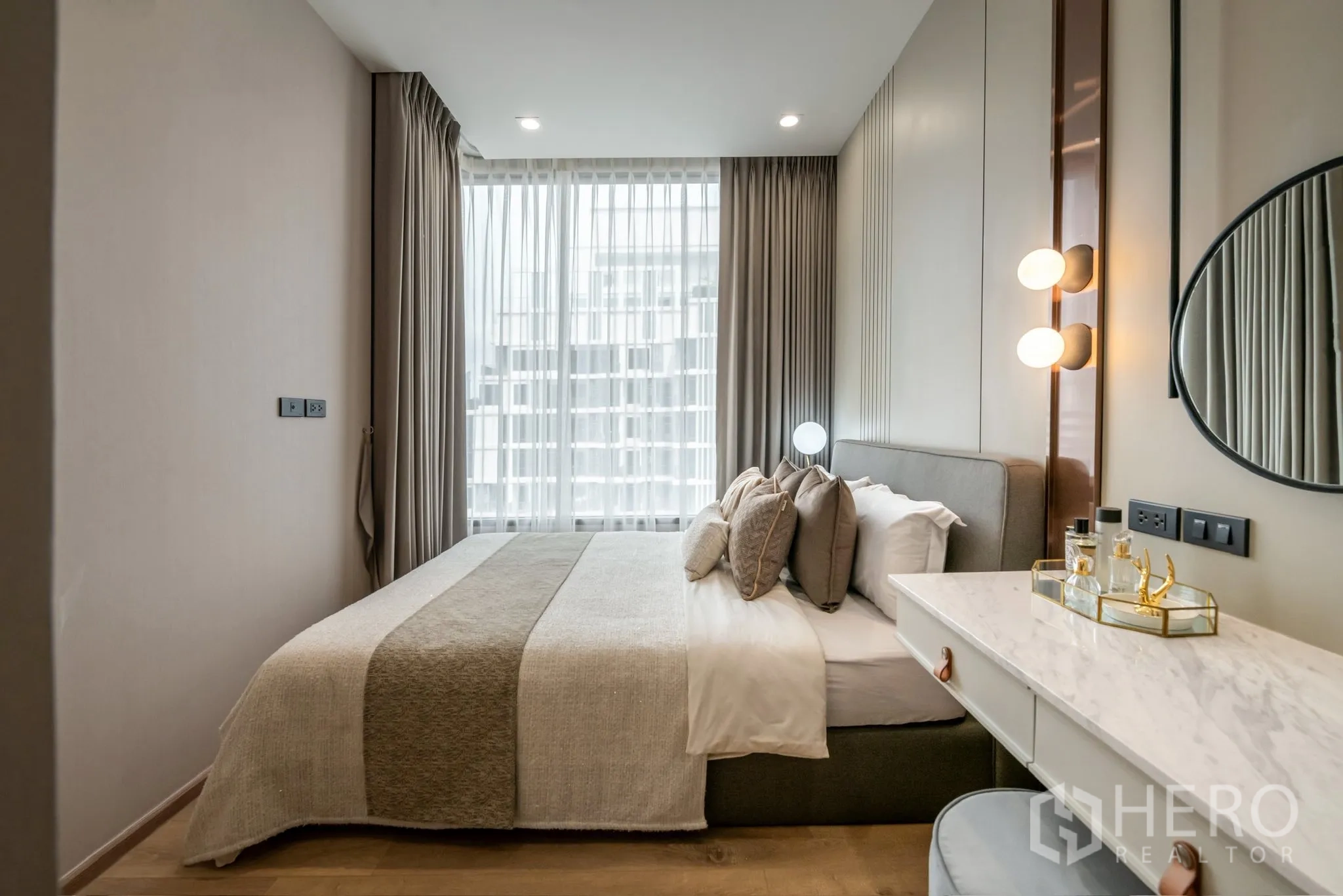 Condominium for rent in Watthana, Bangkok - Cozy bedroom featuring a large floor-to-ceiling window with sheer curtains, upholstered bed, marble-top vanity, and warm bedside lighting.