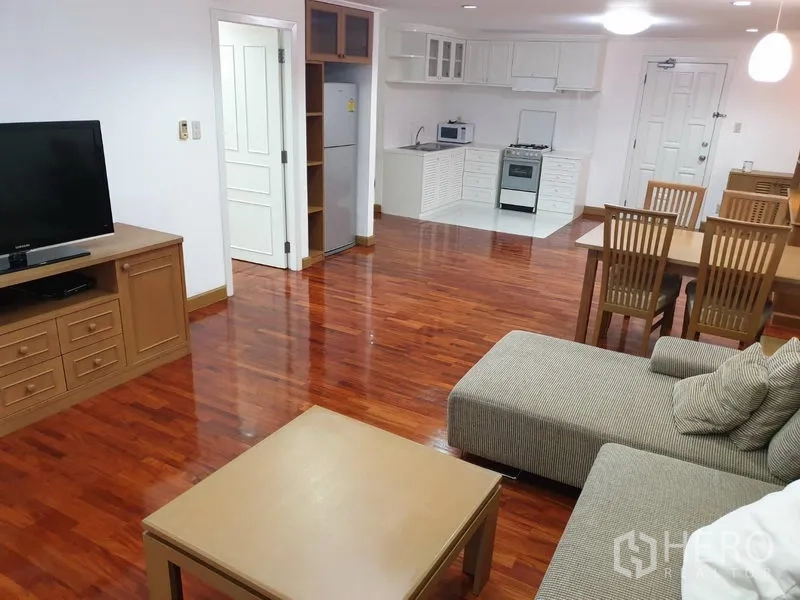 คอนโด ให้เช่าในWatthana, Bangkok - ห้องนั่งเล่นและทานอาหารแบบเปิด พื้นไม้จริง โซฟา ทีวี และครัวขนาดกะทัดรัดที่ Acadamia Grand Tower ใกล้ BTS พร้อมพงษ์