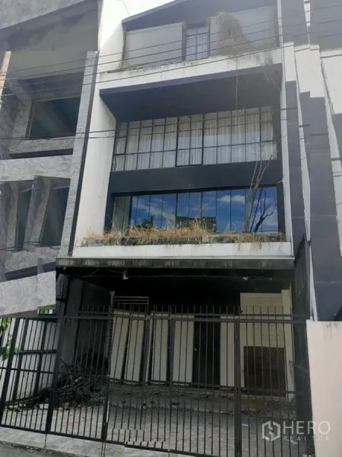 สำนักงานที่บ้าน ให้เช่าในWatthana, Bangkok - ด้านหน้าโฮมออฟฟิศหลายชั้น โทนขาวดำ มีรั้วและที่จอดรถ พร้อมระเบียงปลูกต้นไม้.