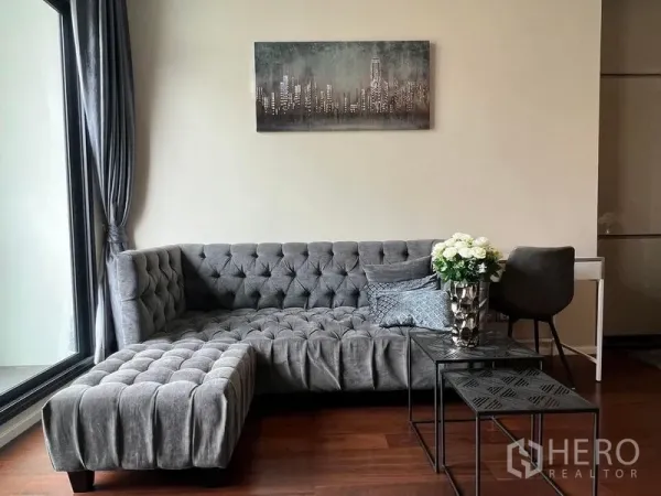 คอนโด ให้เช่าในWatthana, Bangkok - ห้องนั่งเล่นอบอุ่น โซฟากำมะหยี่สีเทาทรงแอล โต๊ะข้าง และหน้าต่างบานใหญ่พร้อมผ้าม่าน
