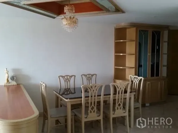 Condominium for rent in Watthana, Bangkok - Dining area with a glass-top table for six under a crystal chandelier and display cabinet.