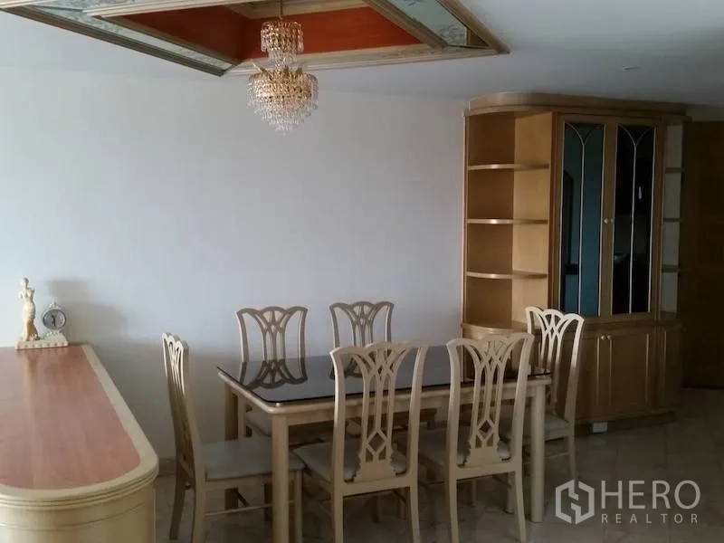 Condominium for rent in Watthana, Bangkok - Dining area with a glass-top table for six under a crystal chandelier and display cabinet.