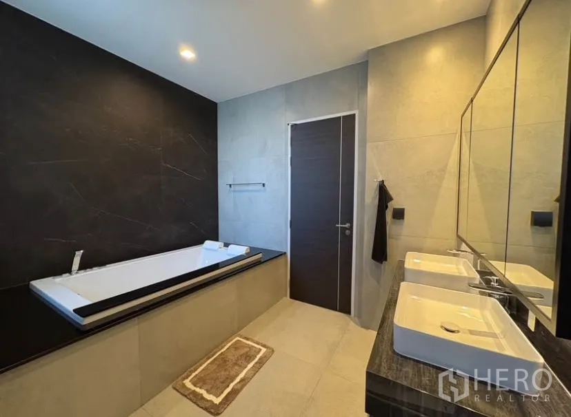 Detached House for rent in Suan Luang, Bangkok - Luxury bathroom featuring a long soaking tub and twin basins against a dark accent wall.