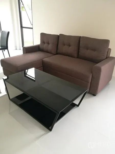 Townhouse for rent in Saphan Sung, Bangkok - Bright living room with an L-shaped brown sofa and black glass coffee table.