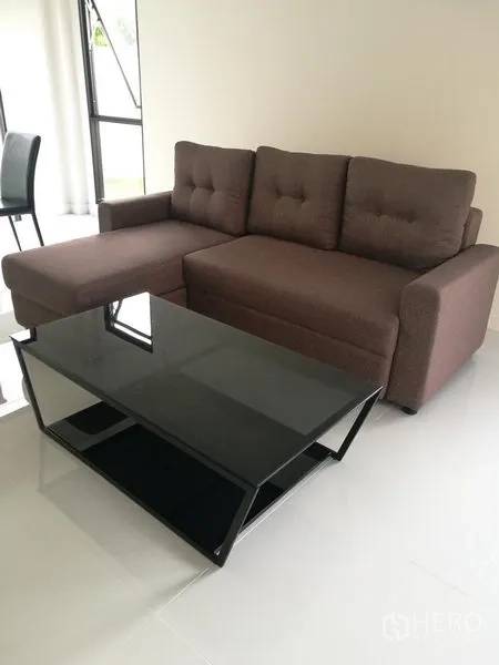 Townhouse for rent in Saphan Sung, Bangkok - Bright living room with an L-shaped brown sofa and black glass coffee table.