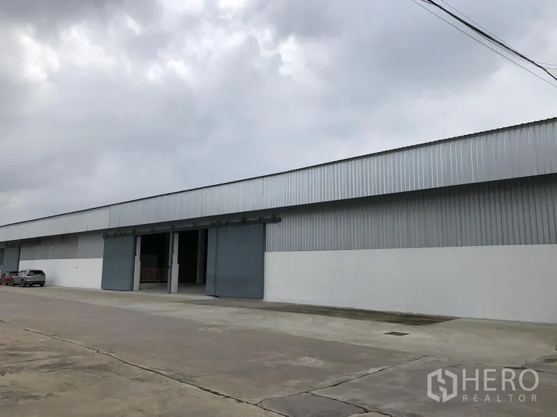 Warehouse for rent in Nonthaburi - Long side facade of the corrugated metal warehouse with multiple bays along an access road.