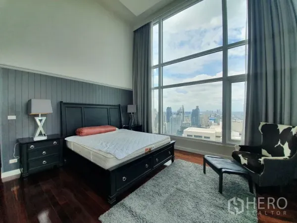 คอนโด ให้เช่าในRatchathewi, Bangkok - ห้องนอนกว้าง เฟอร์นิเจอร์โทนเข้ม พรม และวิวสกายไลน์ผ่านหน้าต่างสูงโปร่ง.