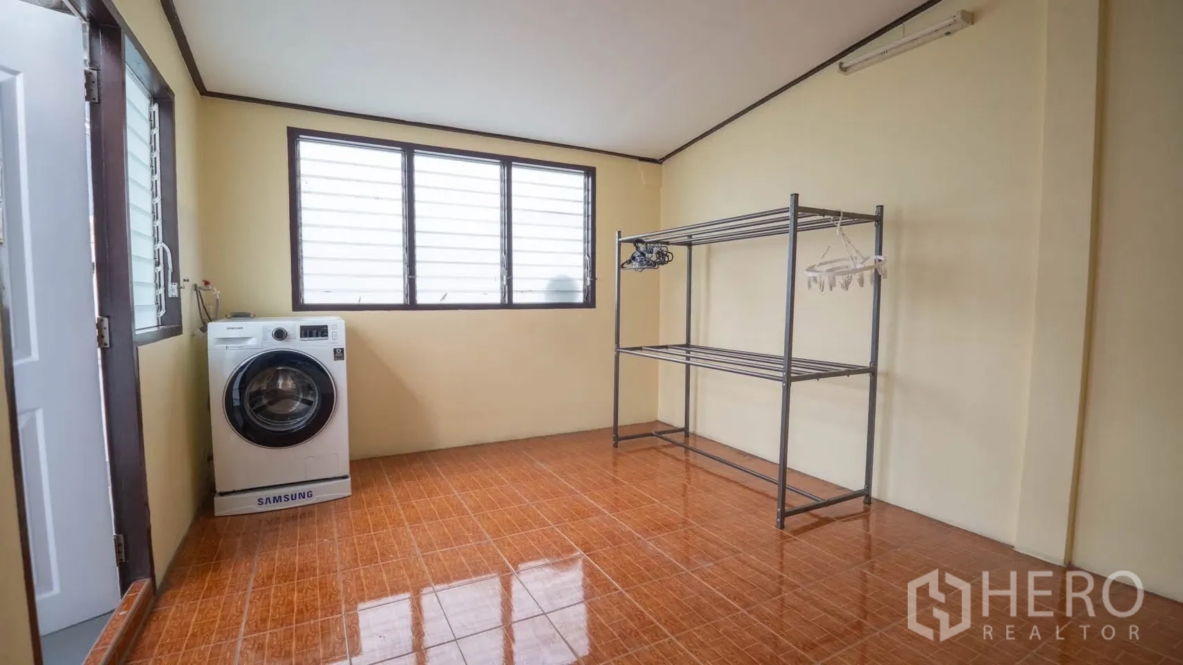 Townhouse for rent in Watthana, Bangkok - Laundry room with a Samsung front-load washer, louvered windows, and metal drying rack on tiled floor.