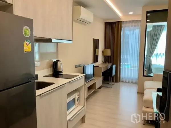 Condominium for sale in Khlong Toei, Bangkok - Open-plan living with built-in kitchen, sofa, desk and floor-to-ceiling window to the bedroom.