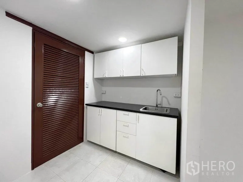 办公空间 出租在Phaya Thai, Bangkok - 紧凑茶水间，白色橱柜、黑色台面与不锈钢水槽，旁有百叶门。