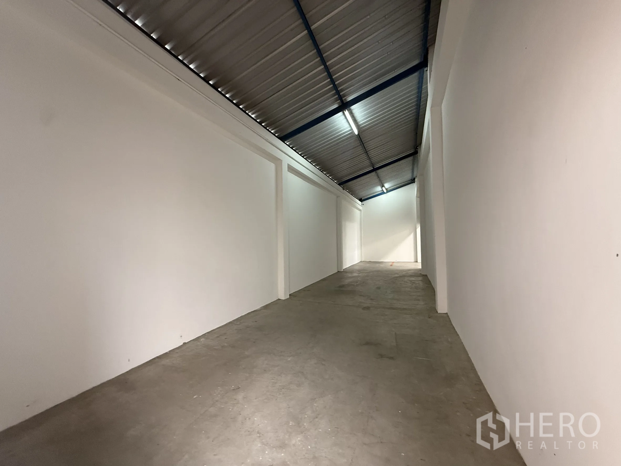 Warehouse for rent or sale in Bang Bo, Samut Prakan - Long auxiliary storage corridor with sloped metal roof and white walls.