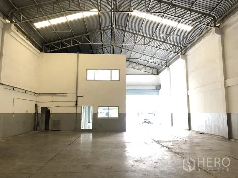 Factory for rent in Pathum Thani - Warehouse interior showing mezzanine office block and large loading door.