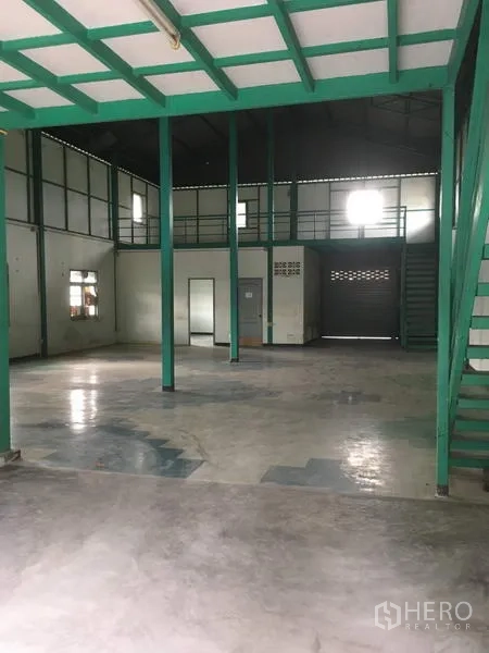 Warehouse for rent in Saphan Sung, Bangkok - Spacious warehouse interior with green steel columns, mezzanine level, and concrete floor.
