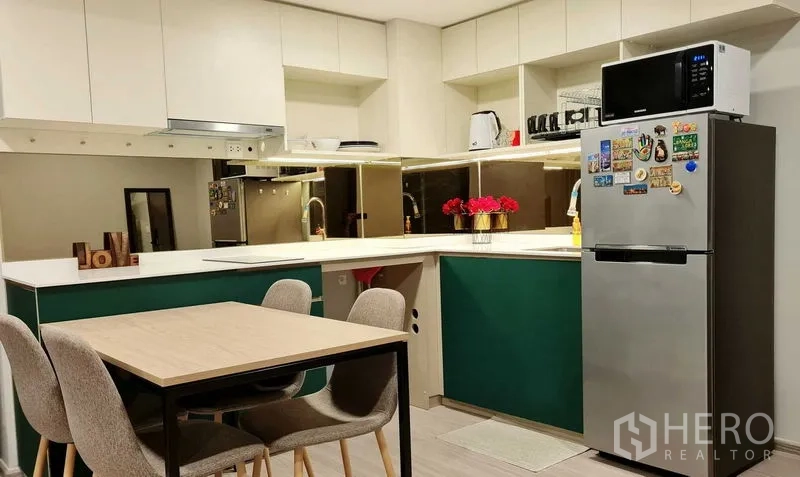 Condominium for rent in Phra Khanong, Bangkok - Contemporary kitchen with white cabinets, green accents, dining set, and full-size fridge.