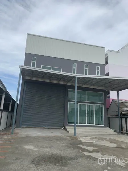 货栈 出租在Prawet, Bangkok - 曼谷Prawet现代两层仓库外观，配有高卷闸门、玻璃办公入口与带顶装卸区及宽阔车道